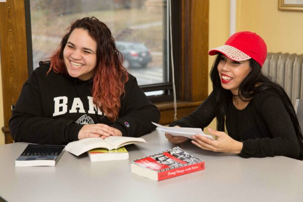Two female students with books and papers smiling and looking up.